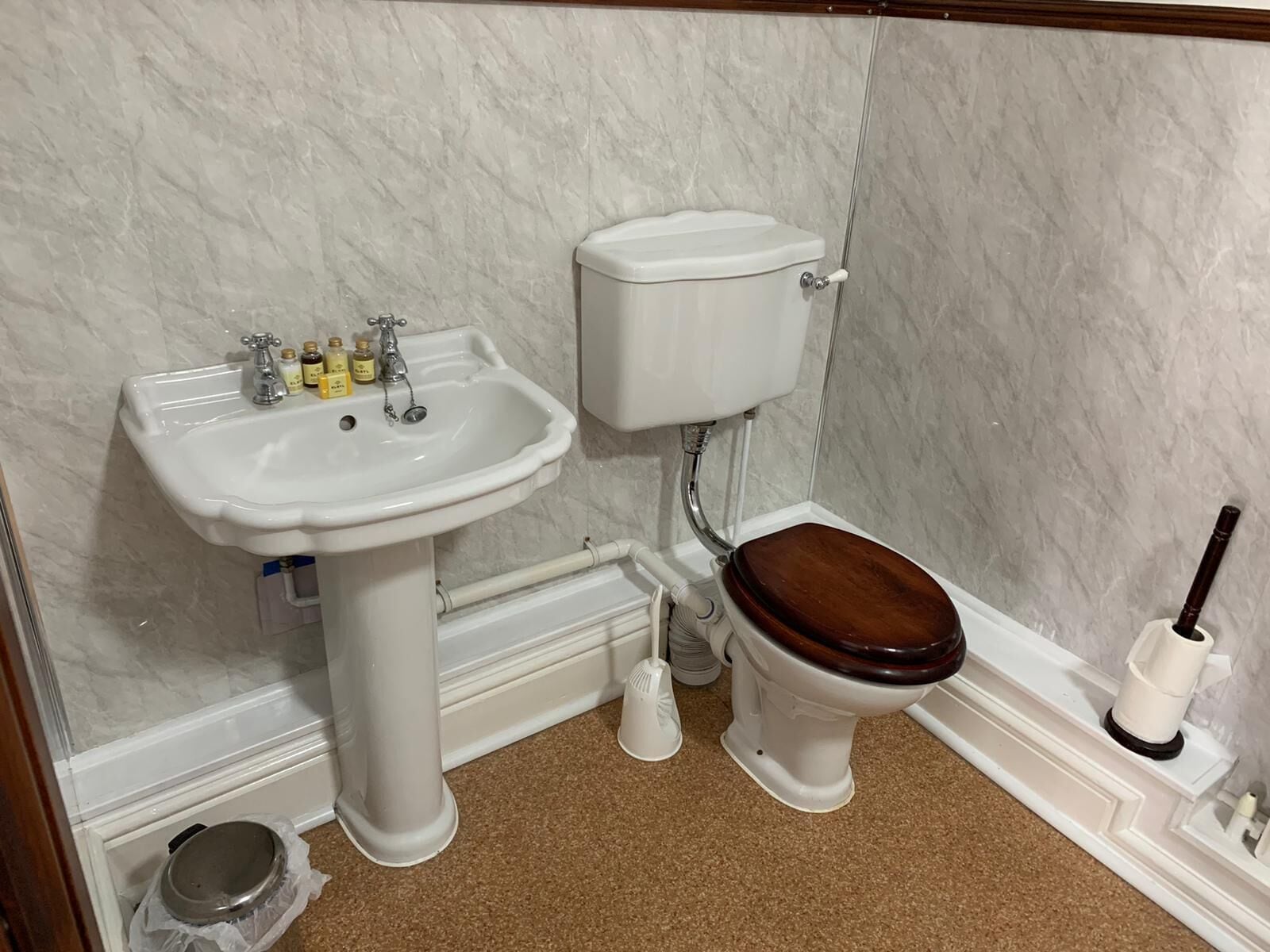 Baño con lavamanos blanco, inodoro y tapa de madera.