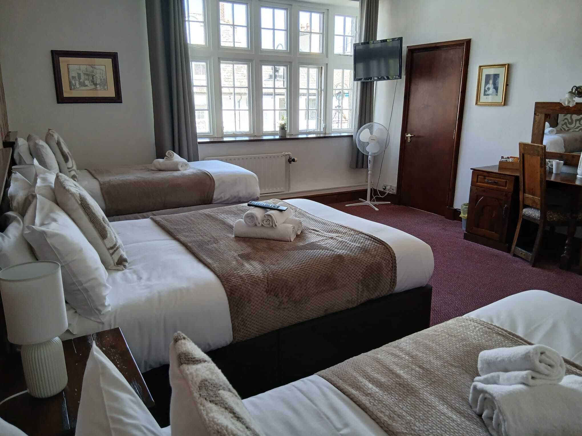 A hotel room with two beds, a desk, a chair, a television, and a window with curtains.