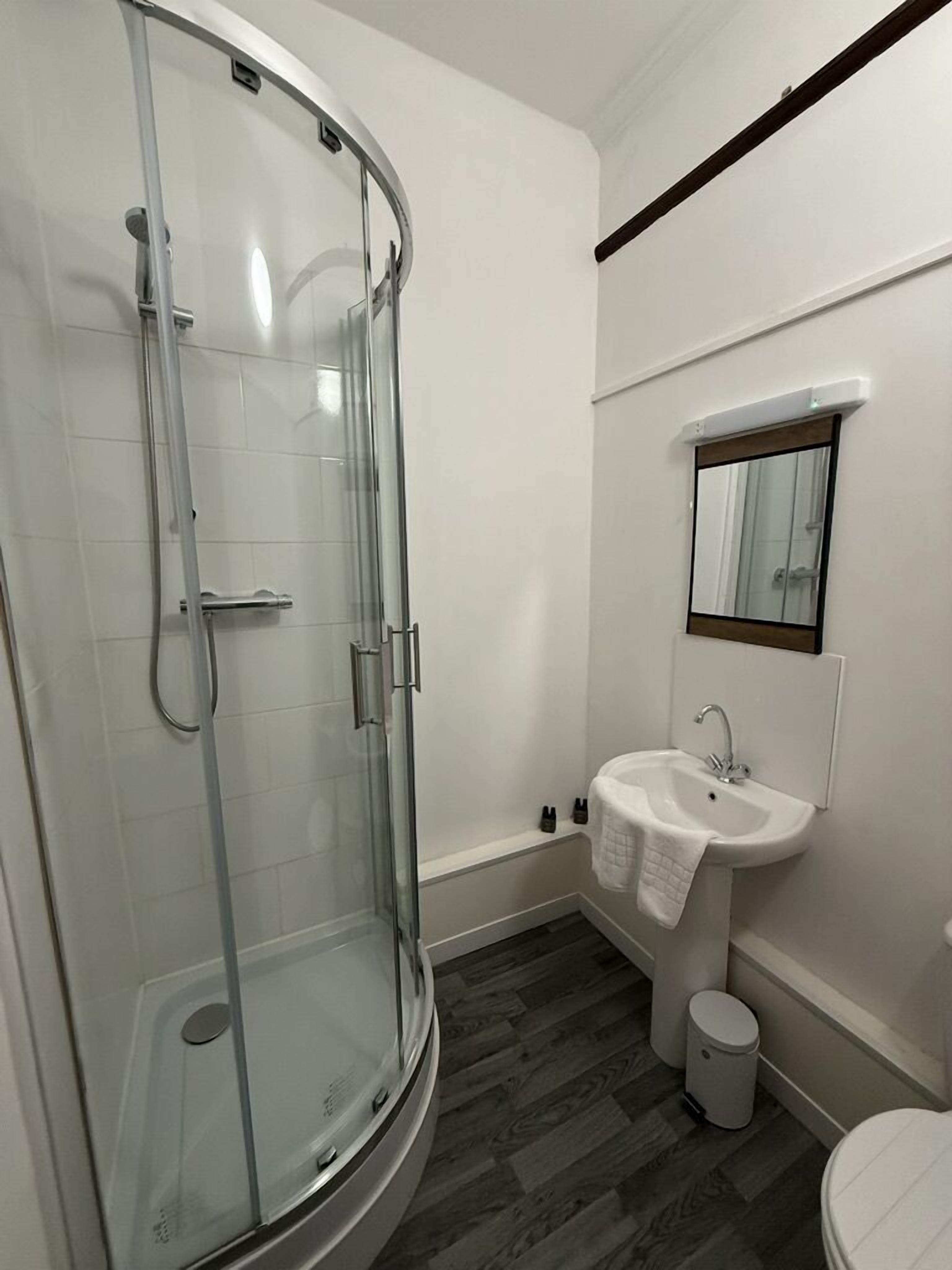 Et moderne badeværelse med et glasafskærmet brusebad, et konsolbord med vask og et toilet.
