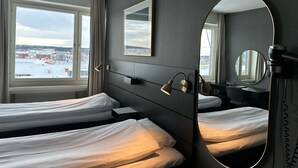Habitación de hotel con dos camas, un espejo grande y vistas a un paisaje nevado a través de la ventana.