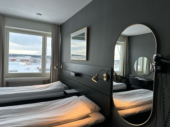Habitación de hotel con dos camas, un espejo grande y vistas a un paisaje nevado a través de la ventana.