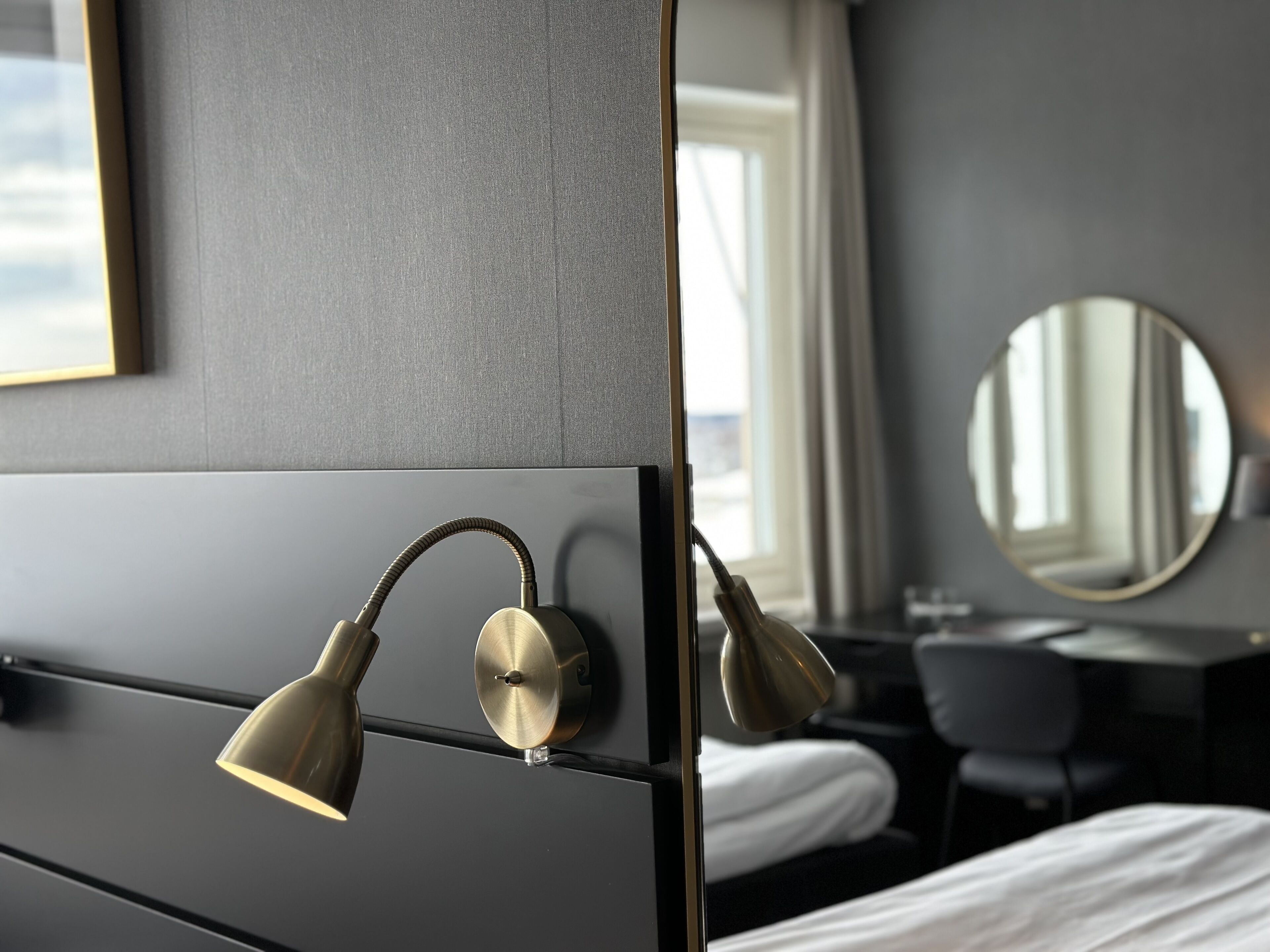 Una habitación de hotel con cama, escritorio y espejo redondo en la pared.