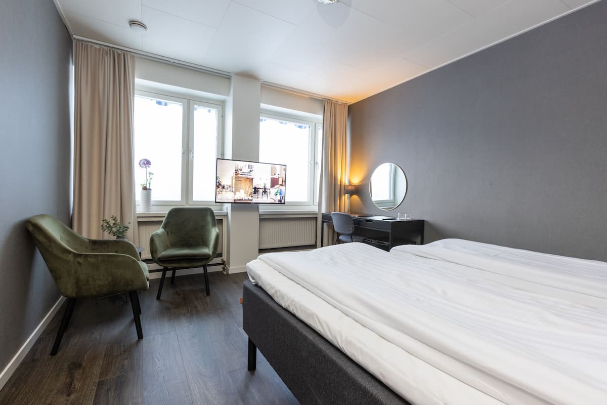 A hotel room with a bed, a desk, a chair, a mirror, and a window with curtains.