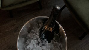 Una habitación con dos sillones verdes, una mesita redonda con una botella de champán y copas, y un balde de metal lleno de hielo.