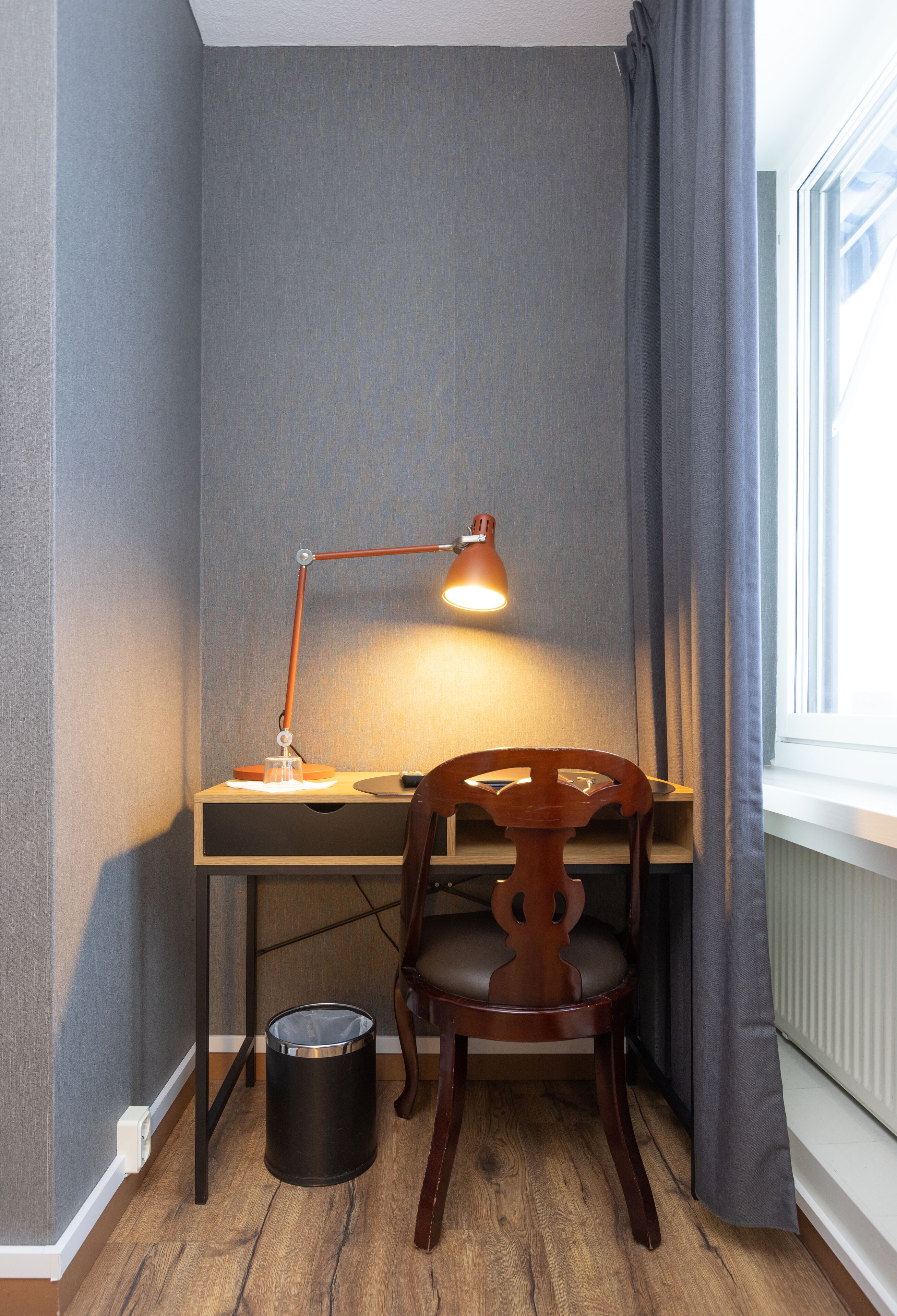 Un espace de travail d’angle comprenant un bureau, une chaise, une lampe et une corbeille.