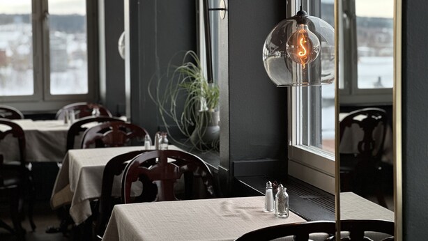 Un restaurante con mesas dispuestas para comer, una planta en maceta y una bombilla encendida en la pared.