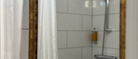 A bathroom with white tiled walls, a shower with a handheld showerhead, and a towel rack.