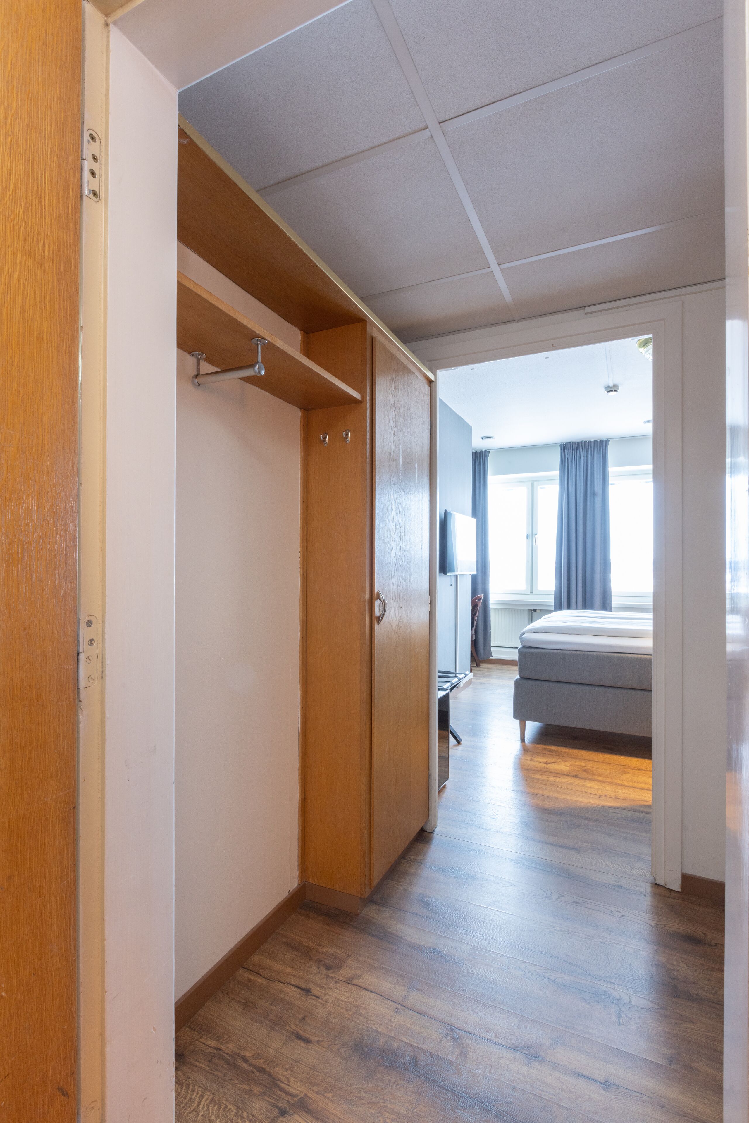 Ett hotellrum med en garderob i trä, en säng, en tv och ett fönster med gardiner.