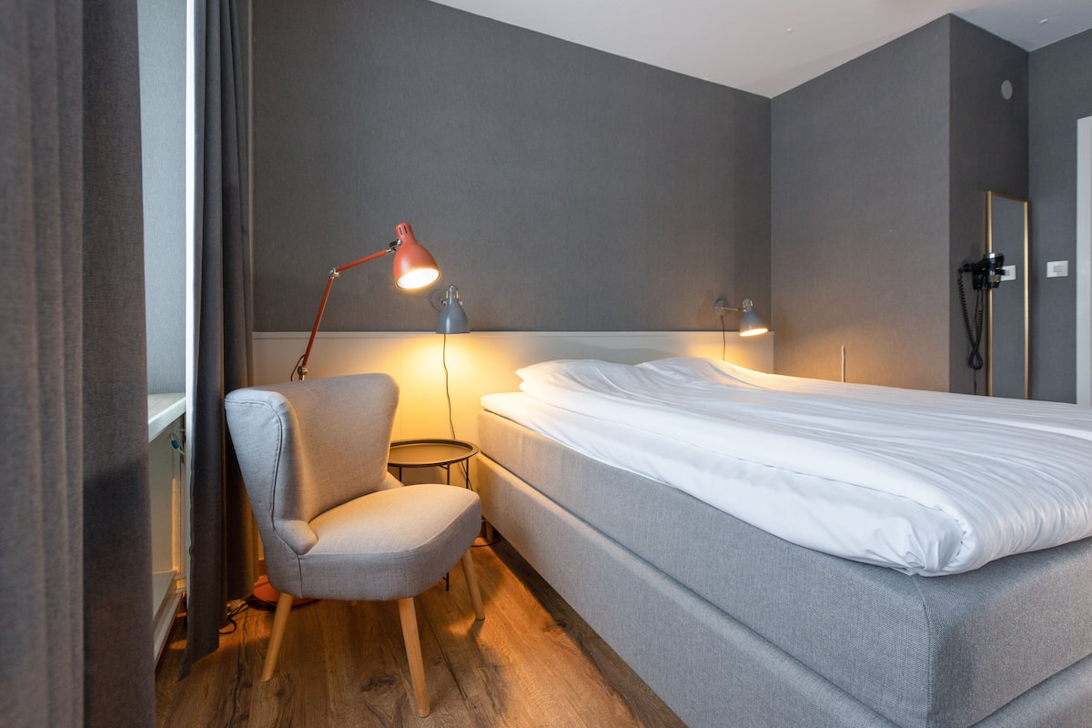 A hotel room with a bed, a chair, and a desk with a lamp.