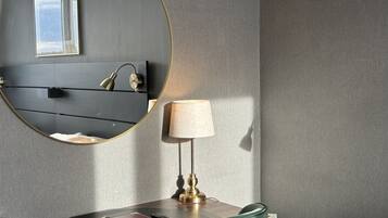 A modern hotel room with a round mirror, a desk with a lamp, a chair, and a television.
