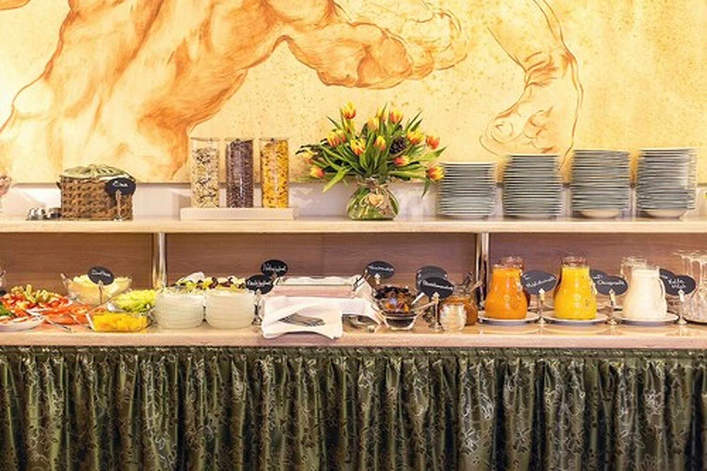 A buffet setup with various food items and condiments, including salads, fruits, and beverages, arranged on a table with a green tablecloth.