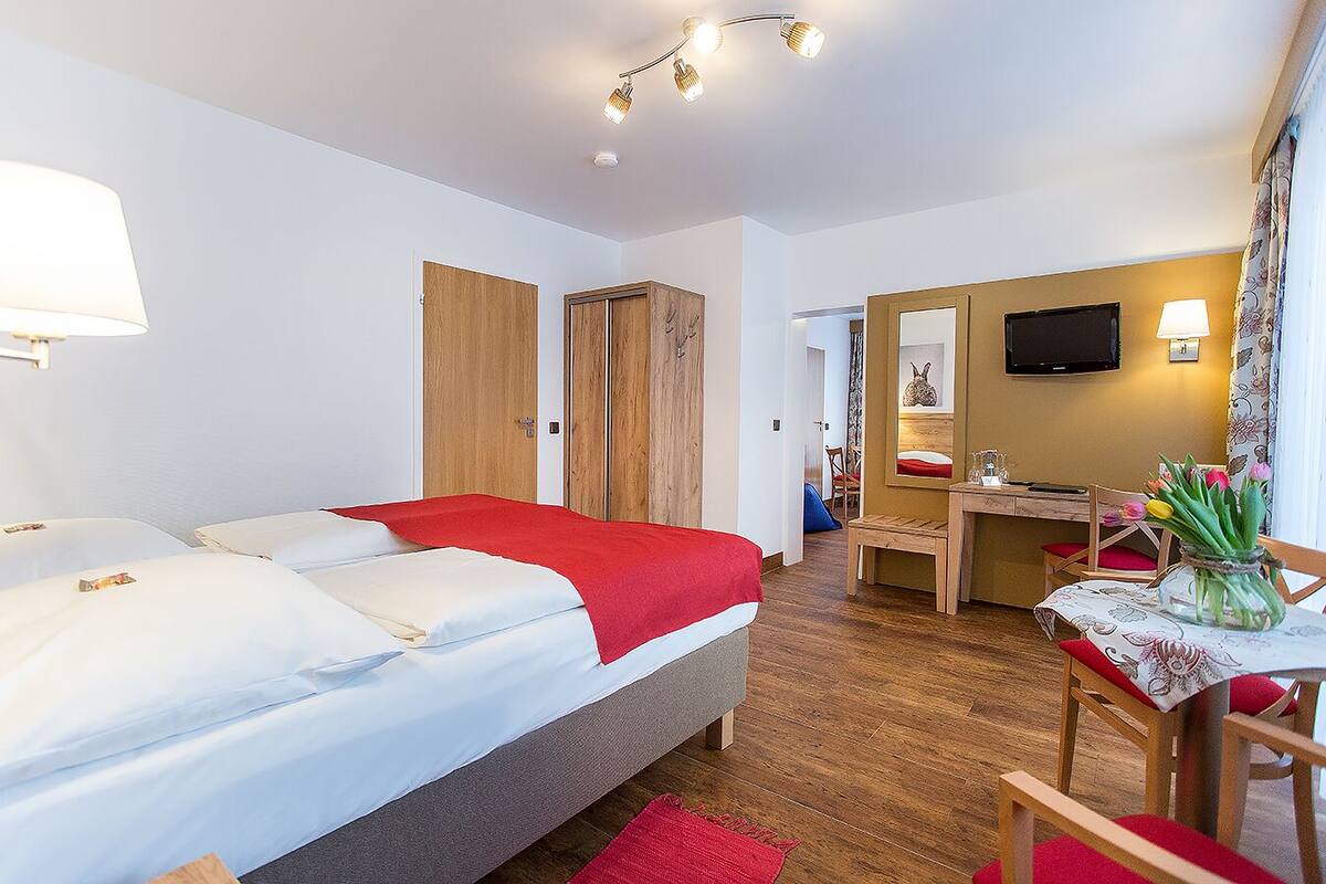 A hotel room with a bed, a desk, a chair, a mirror, and a television.