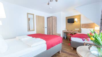 Quarto de hotel com duas camas, uma escrivaninha, televisão e uma pequena mesa com flores.