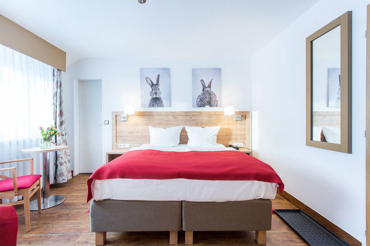 A hotel room with a bed, bedside tables, a mirror, and a window with curtains.
