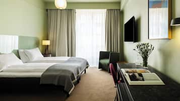Een hotelkamer met een bed, een bureau met stoel, een televisie, een lamp en een raam met gordijnen.