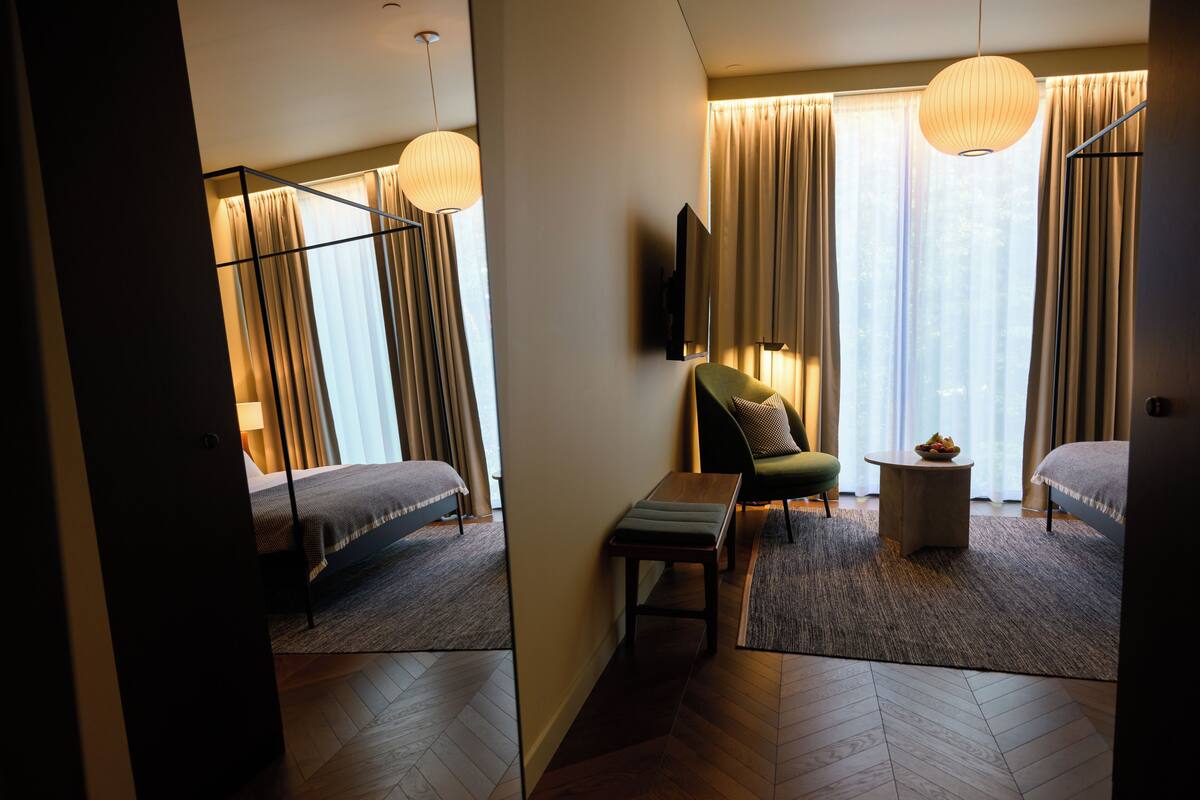 Ein Hotelzimmer mit Bett, Schreibtisch, Stuhl, Fernseher und einem großen Fenster mit Vorhängen.