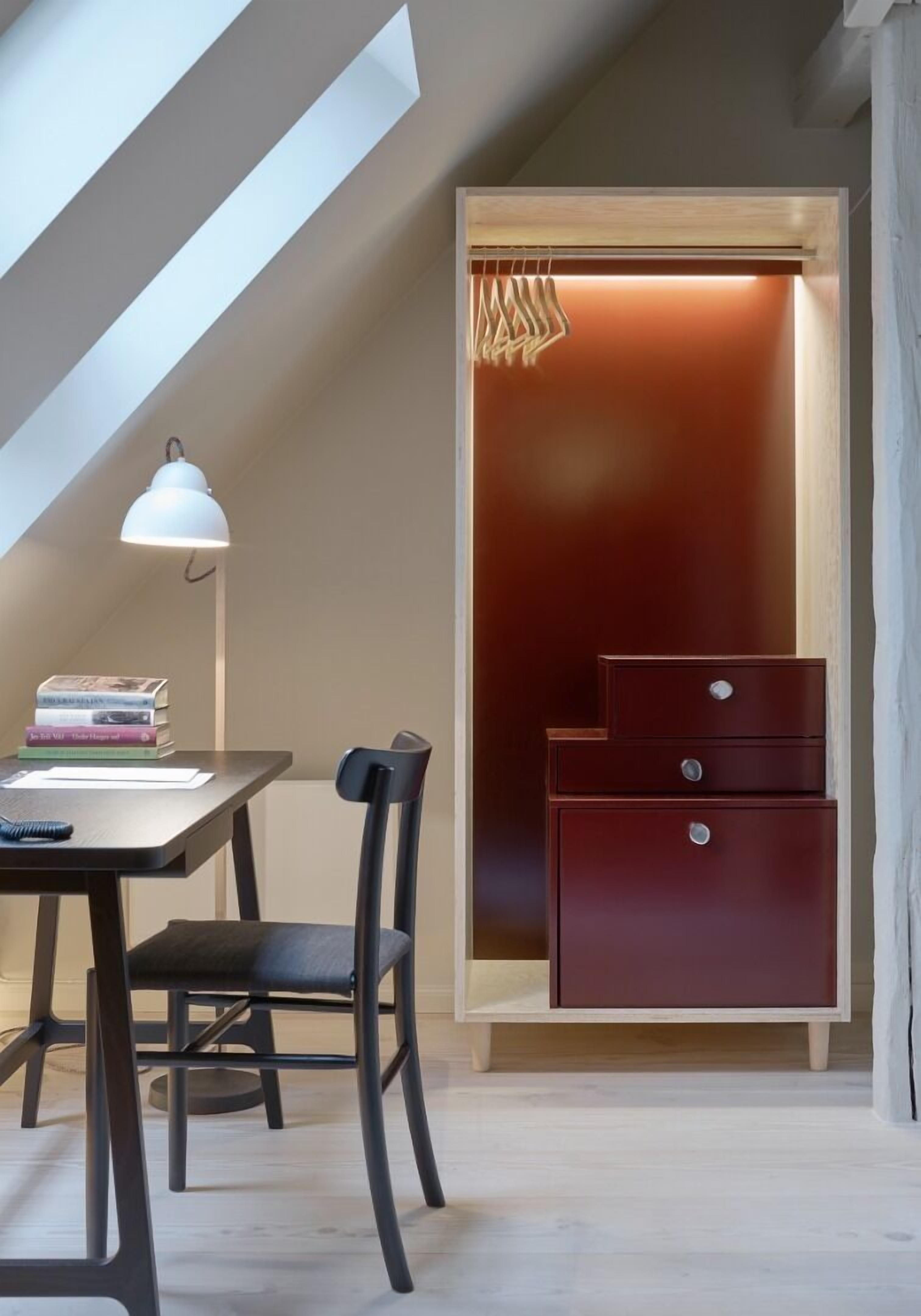 A study with a desk, chair, and books. There is a closet with a hanging rack and a mirror.