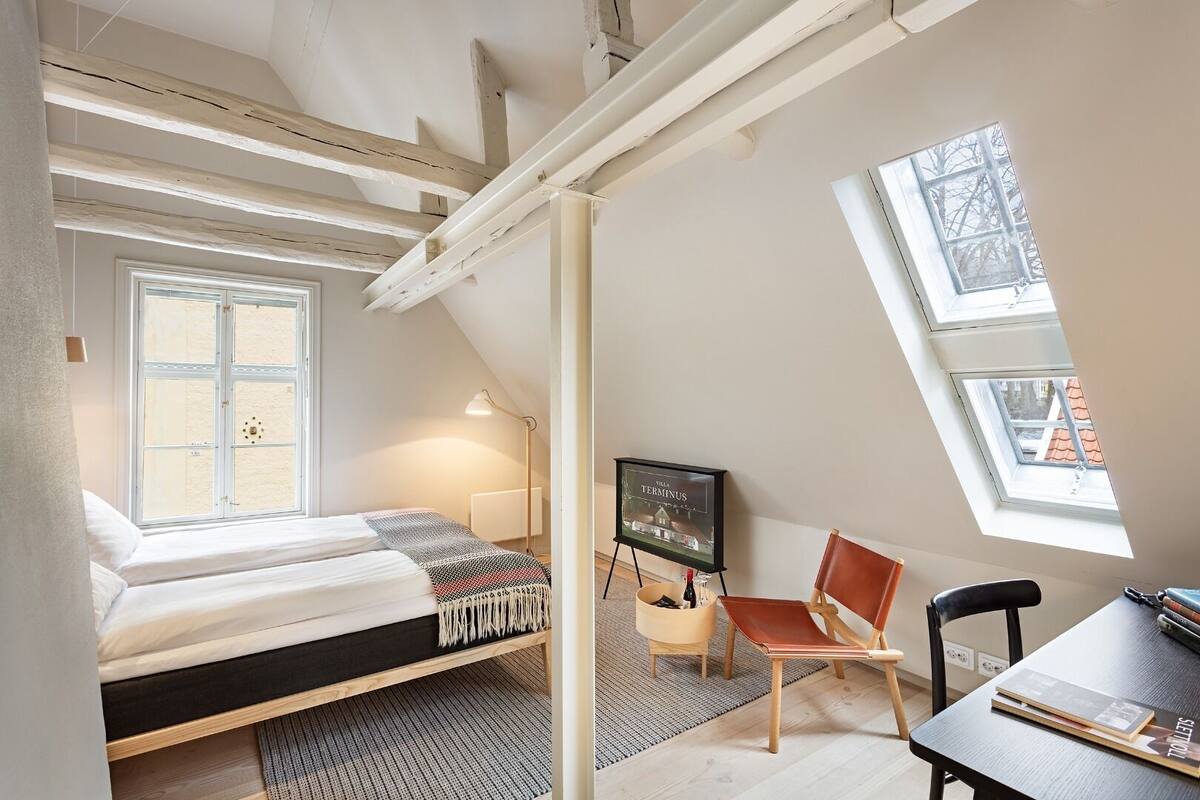 Ein Schlafzimmer im Loft-Stil mit Bett, Schreibtisch, Stuhl, Fernseher und Dachfenster.