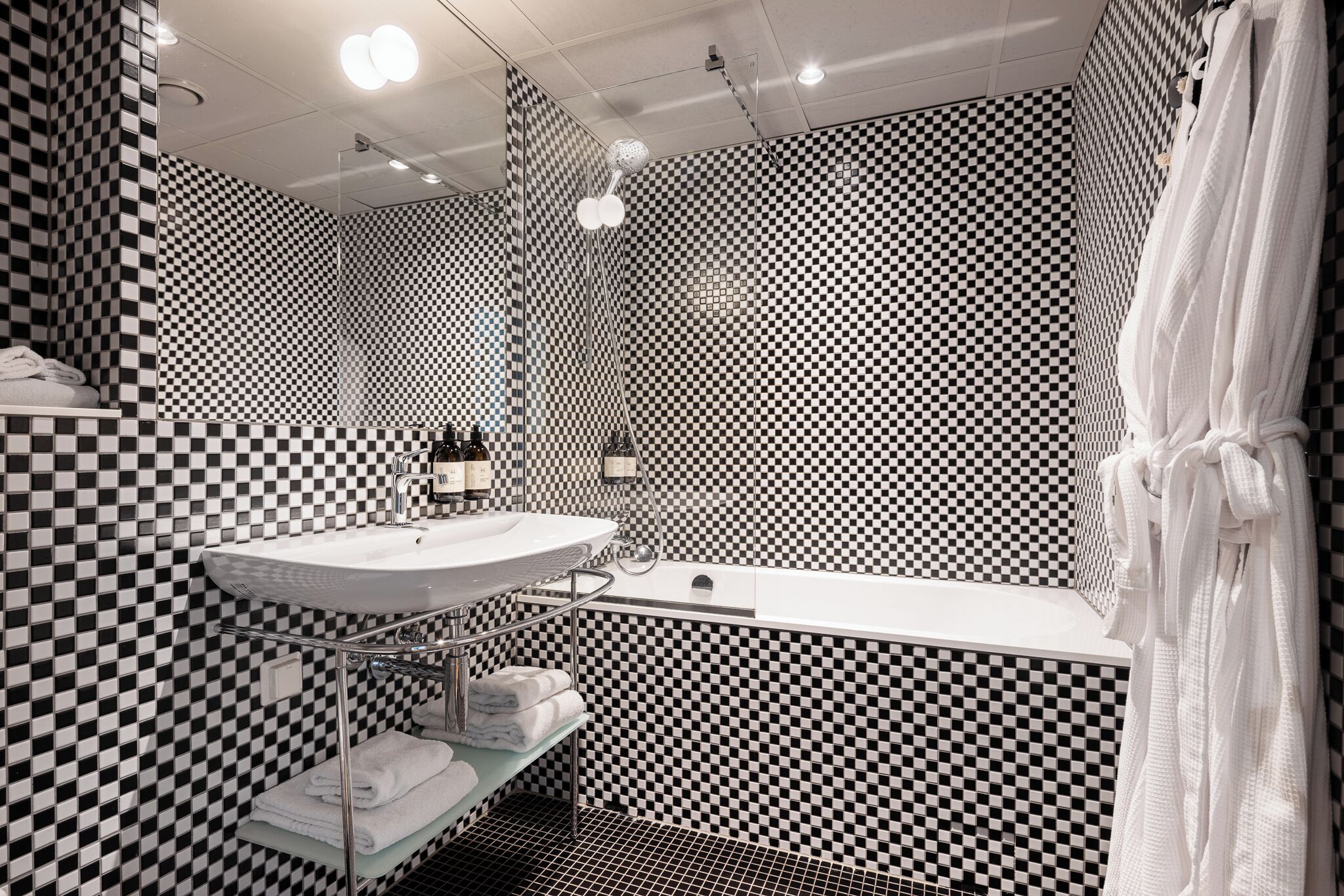 A bathroom with a checkered black and white tile pattern, a white sink, a mirror, and a shower curtain.