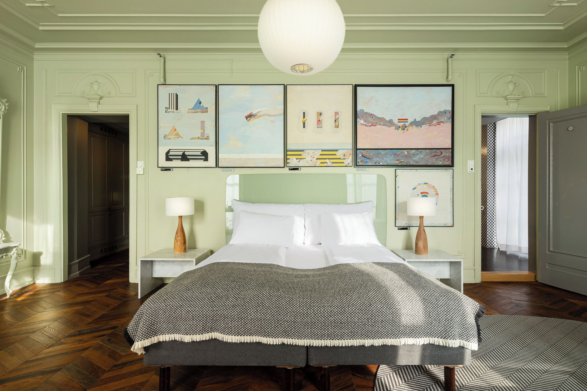 A bedroom with a bed, two bedside tables, a hanging light fixture, and artwork on the wall.