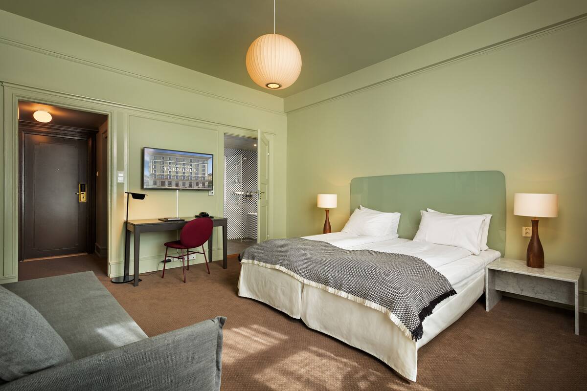 Ein Hotelzimmer mit Bett, Nachttischen, Schreibtisch, Stuhl und einer Pendelleuchte.