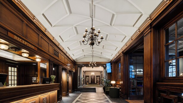A reception area with a chandelier, a reception desk, and a check-in counter. - Grand Hotel Terminus (Bergen)