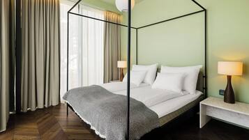 A room with a four-poster bed, a nightstand with a lamp, and a view of the outdoors through sheer curtains.