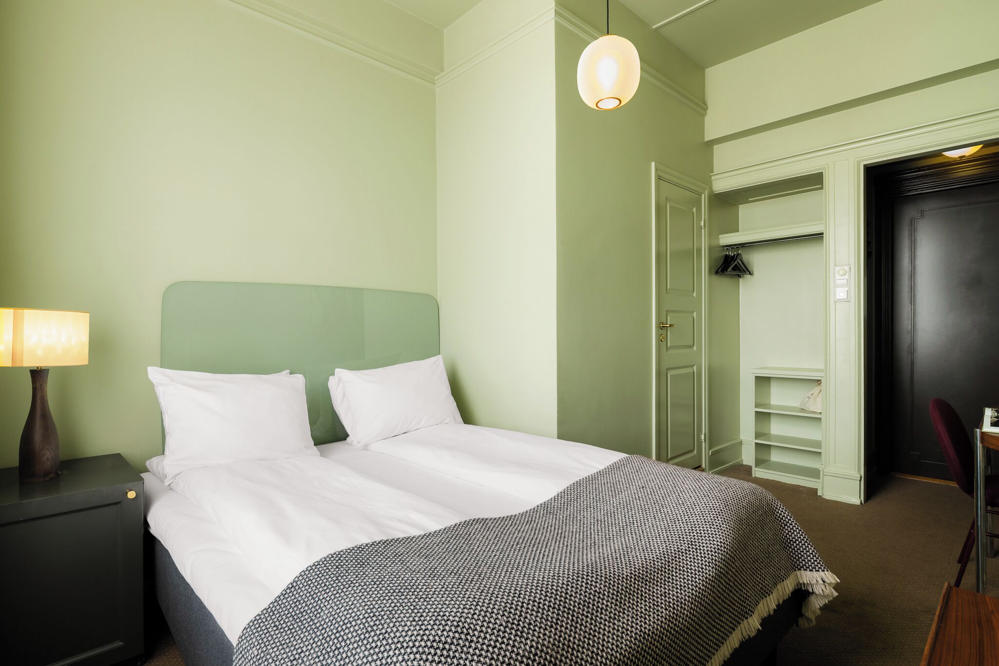 Una habitación de hotel con cama, mesita de noche, lámpara, armario y puerta.