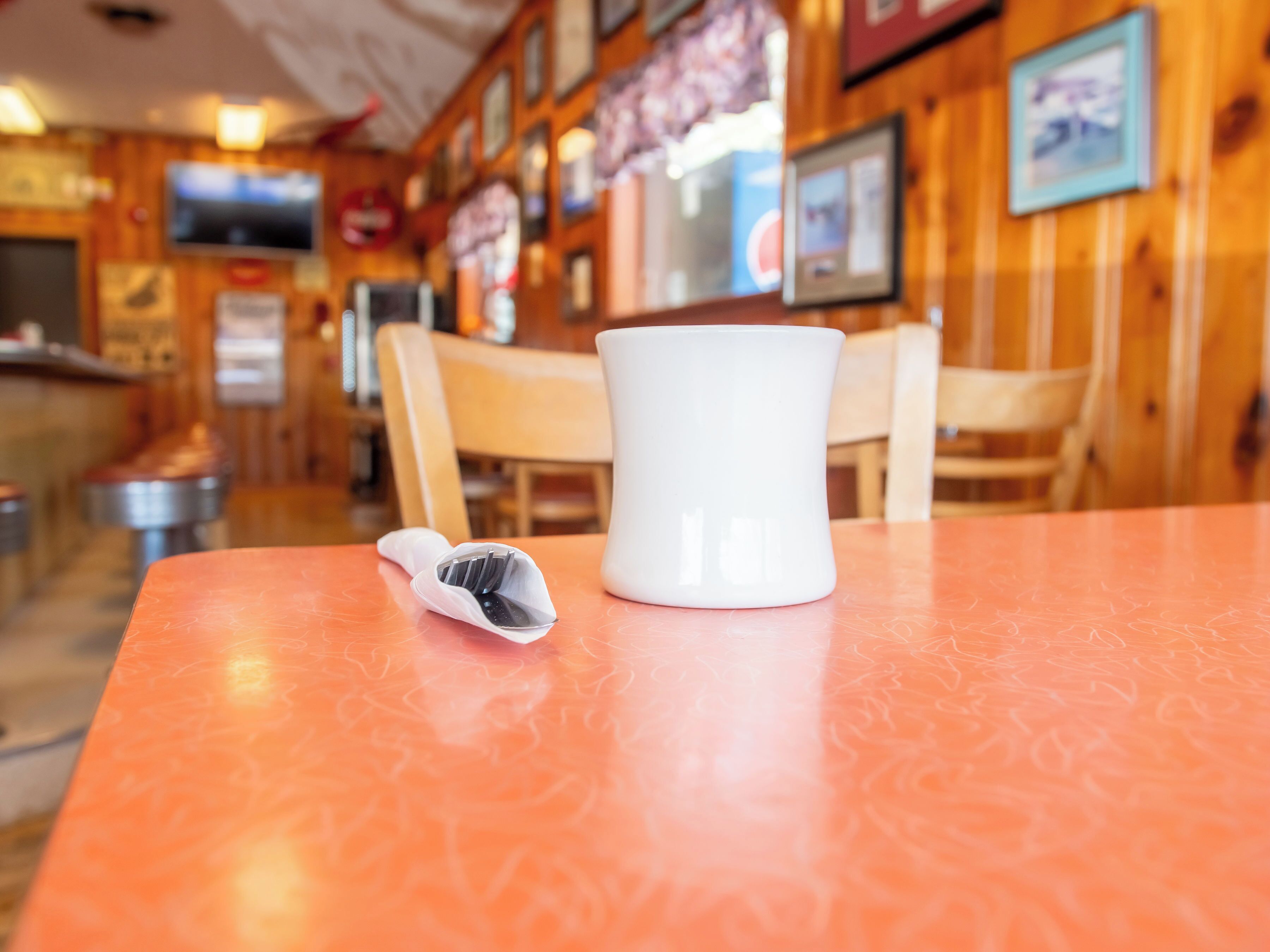 A restaurant interior with wooden walls, a television mounted on the wall, and a table with a white mug and a napkin holder.