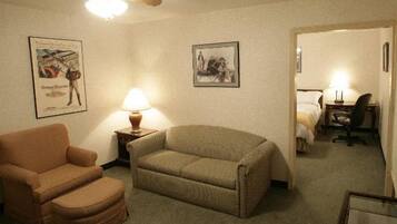 A hotel room with a sofa, armchair, and a desk with a lamp. There are two framed pictures on the wall.