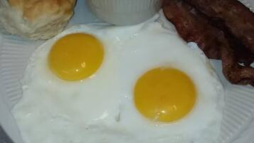A plate with two fried eggs, a biscuit, a bowl of grits, and bacon.