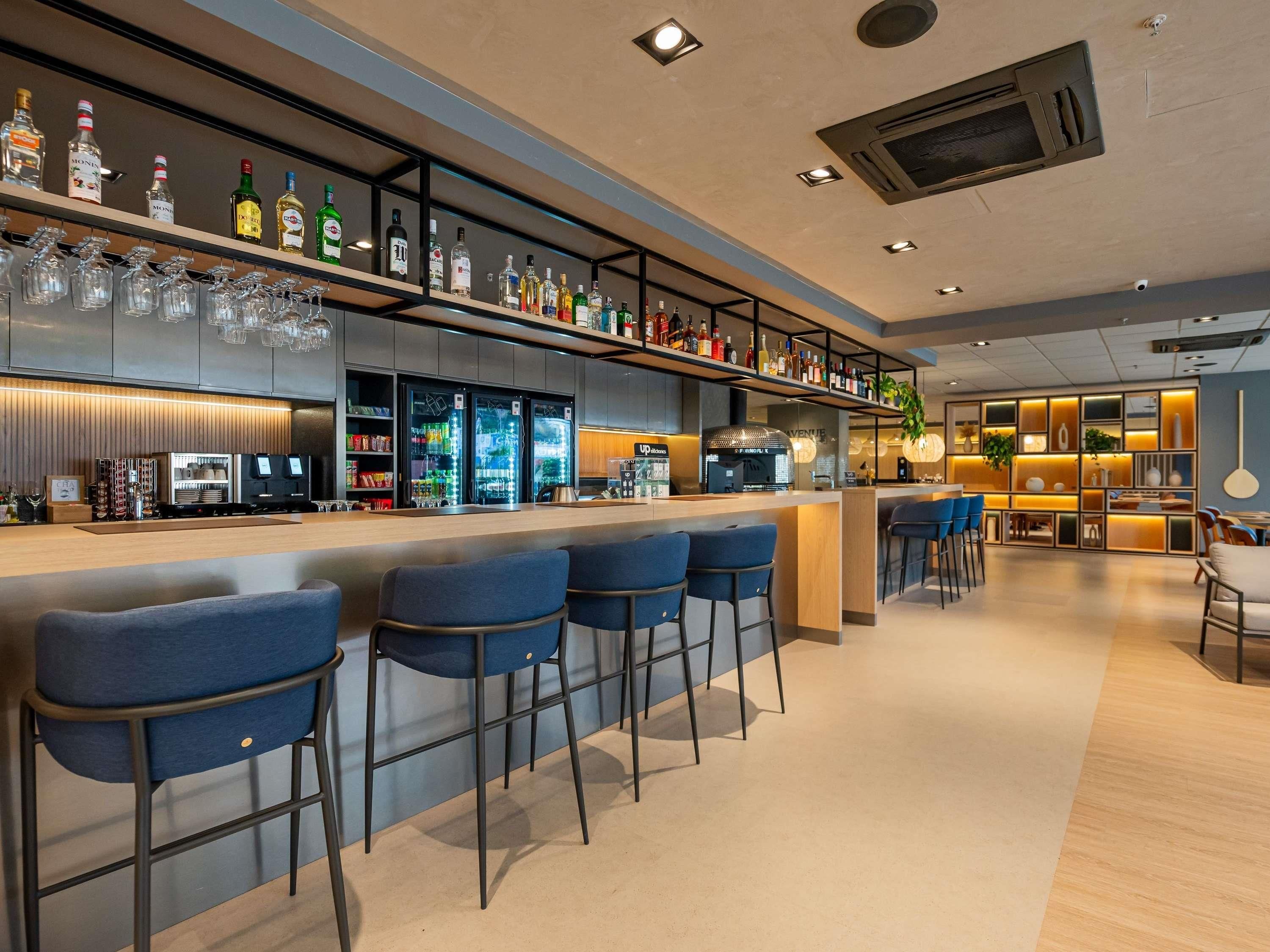 Zona de bar con una barra larga, varios taburetes y una variedad de botellas y vasos en estanterías.