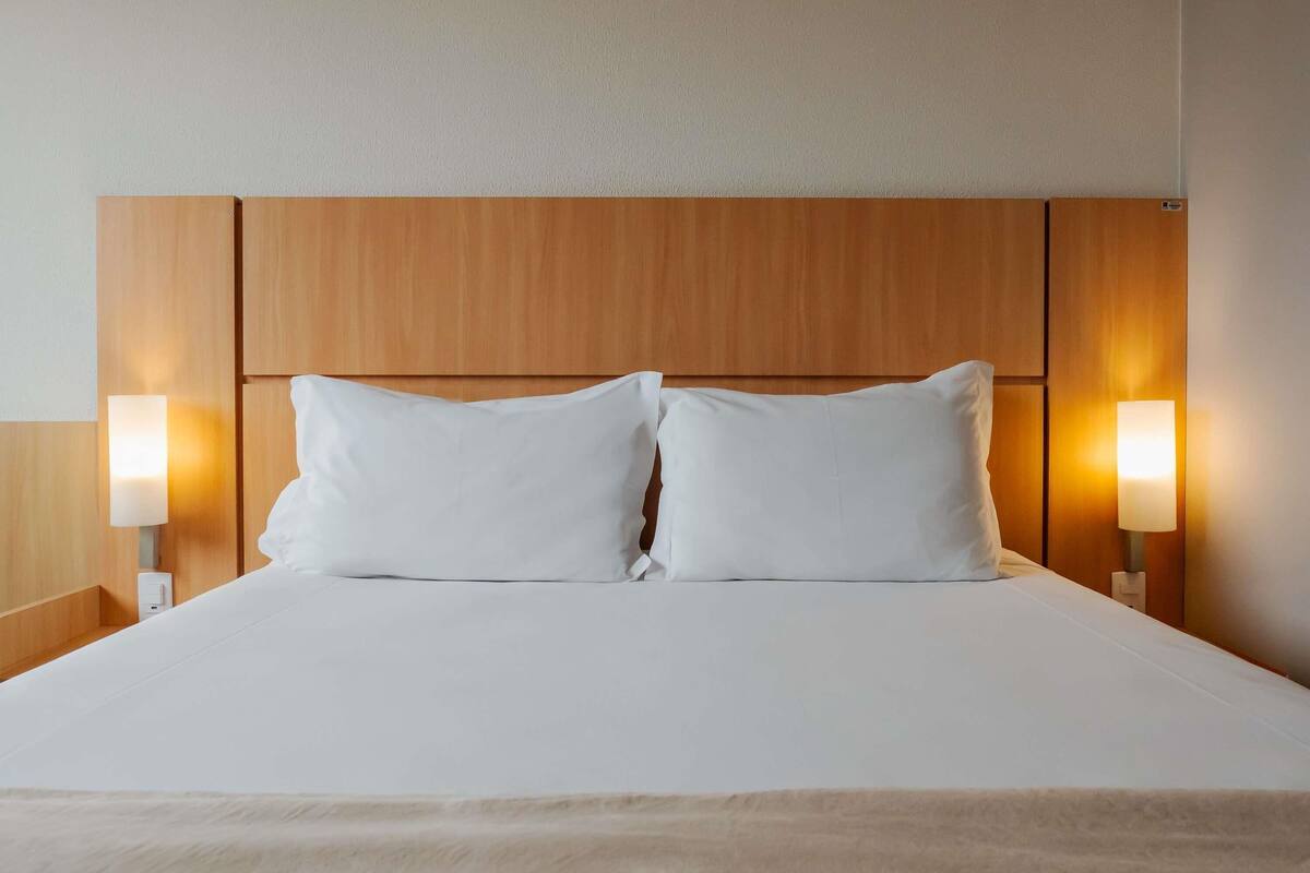 Une chambre d’hôtel avec une tête de lit en bois, deux oreillers blancs et des lampes de chevet.