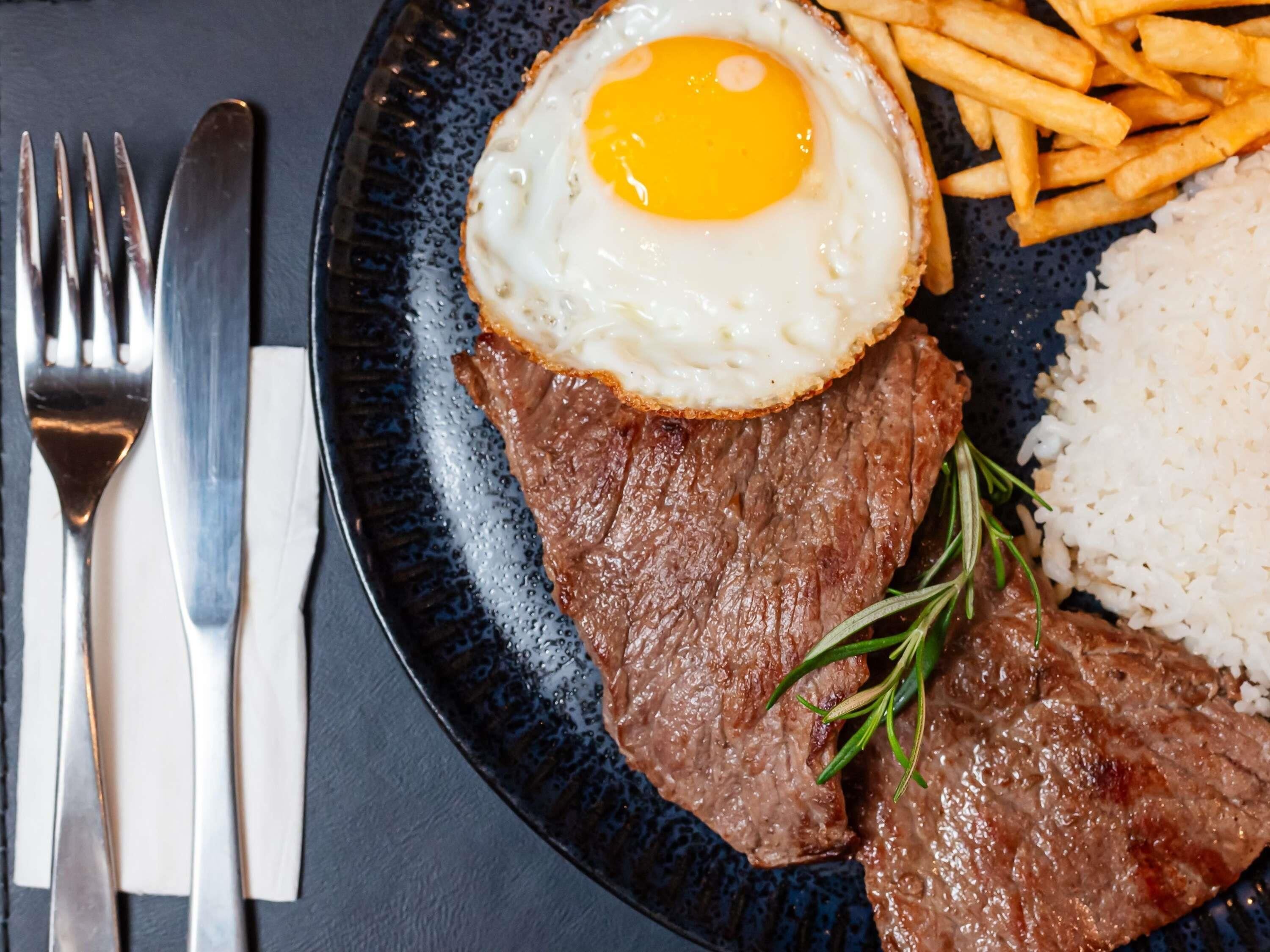 Une assiette avec un steak, un œuf au plat, des frites et du riz.
