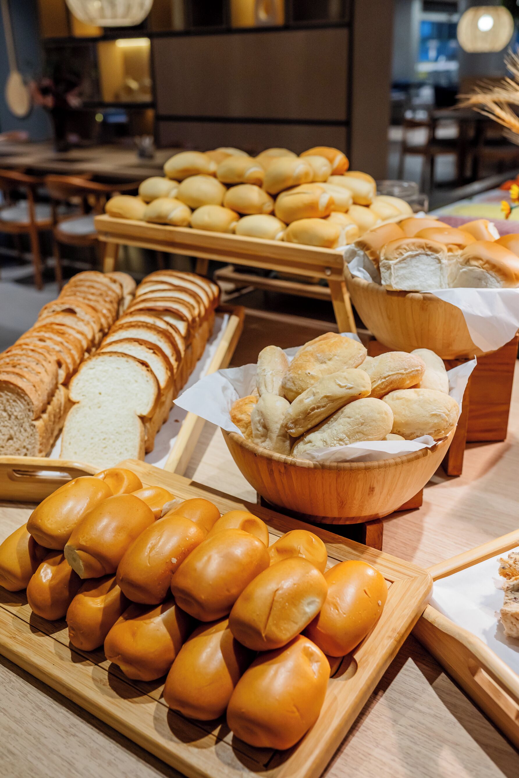 A variety of bread displayed on wooden trays in a bakery setting.