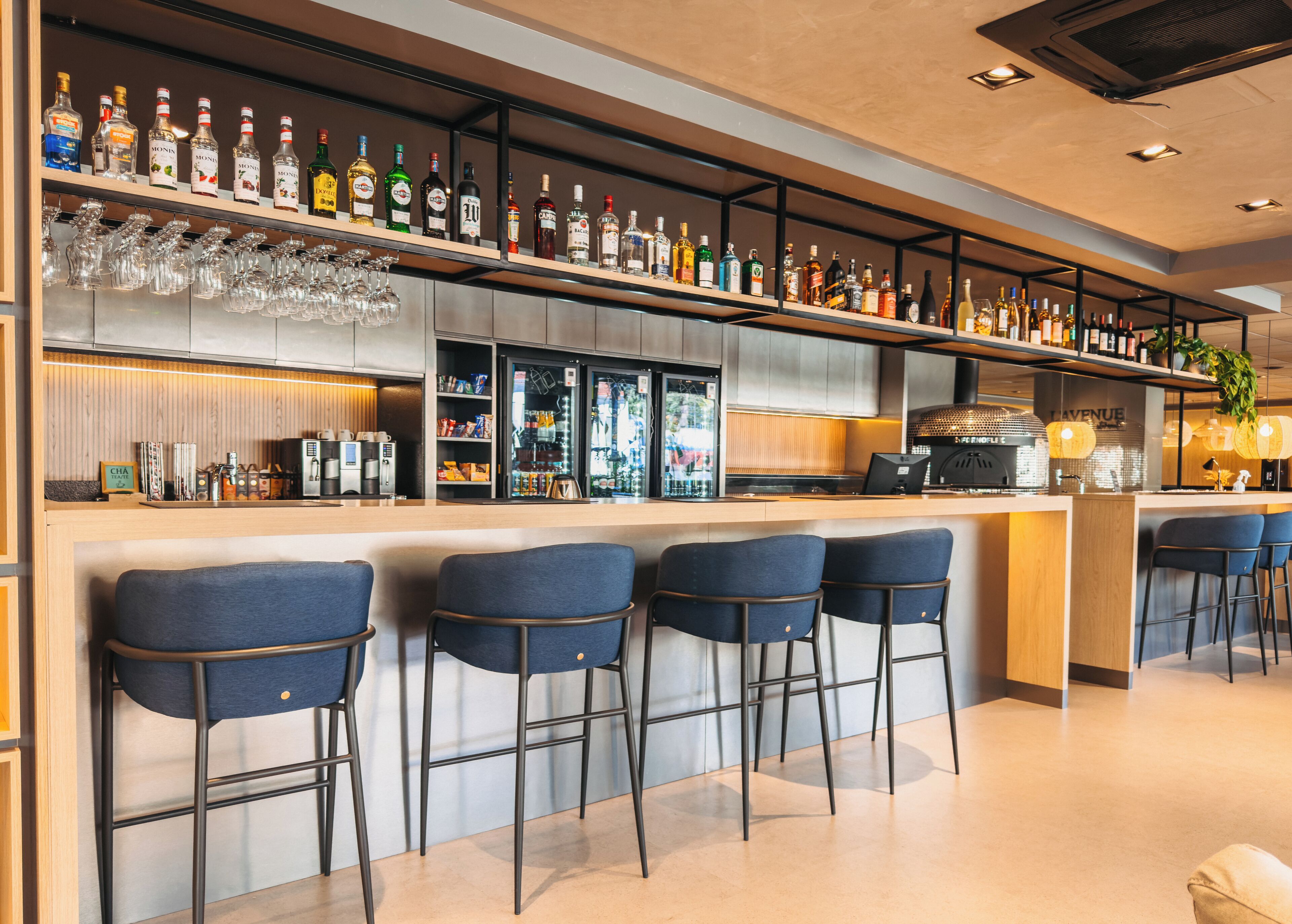 Uma área de bar com várias garrafas de bebidas, copos e uma máquina de café.