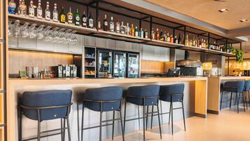 Uma área de bar com várias garrafas de bebidas, copos e uma máquina de café.