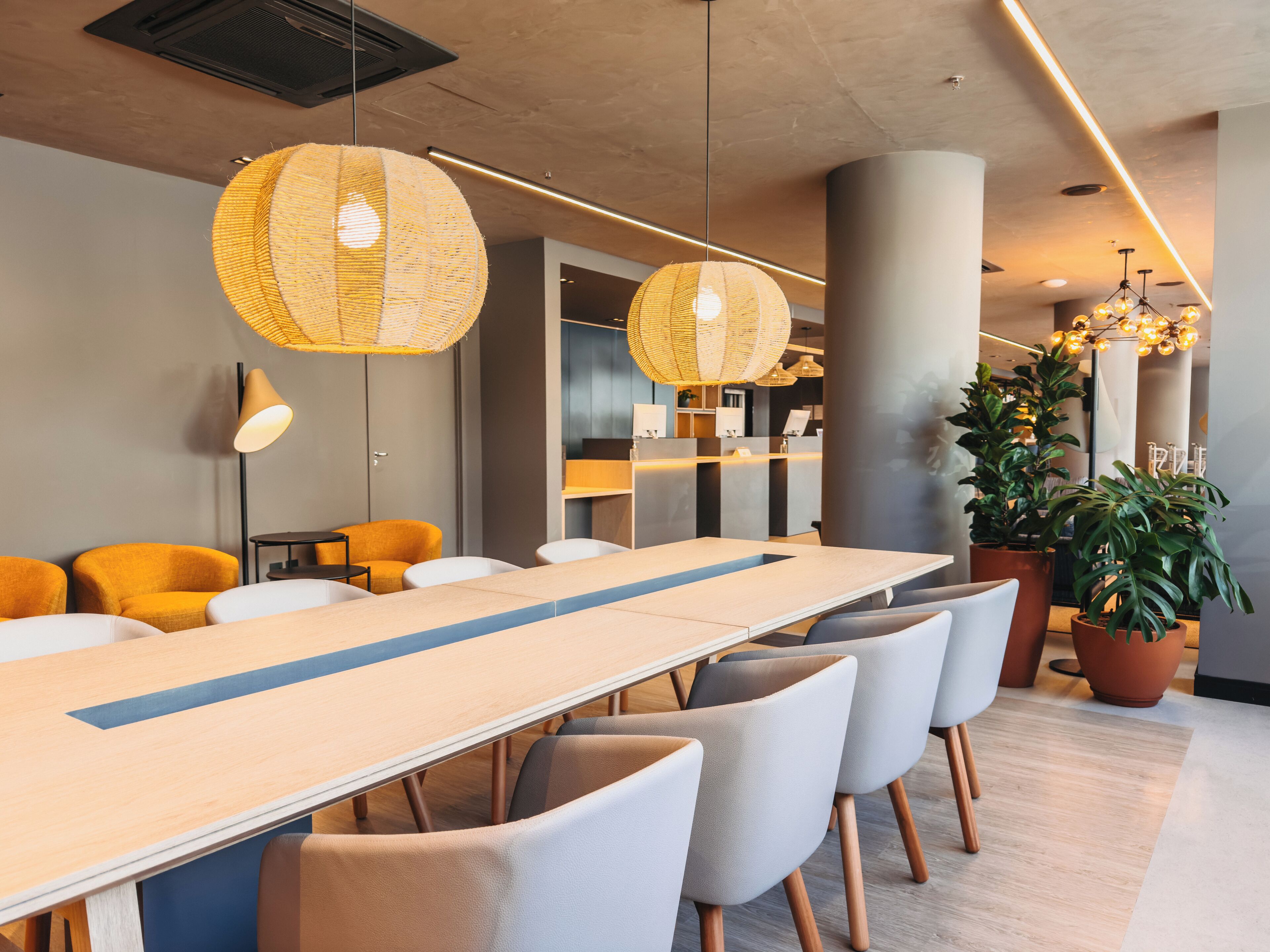A modern conference room with a long table, multiple chairs, and hanging wicker lamps.
