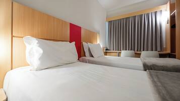 Une chambre d’hôtel avec deux lits, une tête de lit en bois, un mur d’accent rouge, un bureau et une fenêtre avec des rideaux.