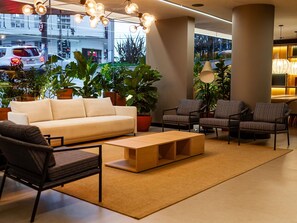 Un vestíbulo moderno con un sofá, sillones, una mesa de centro y plantas en macetas.