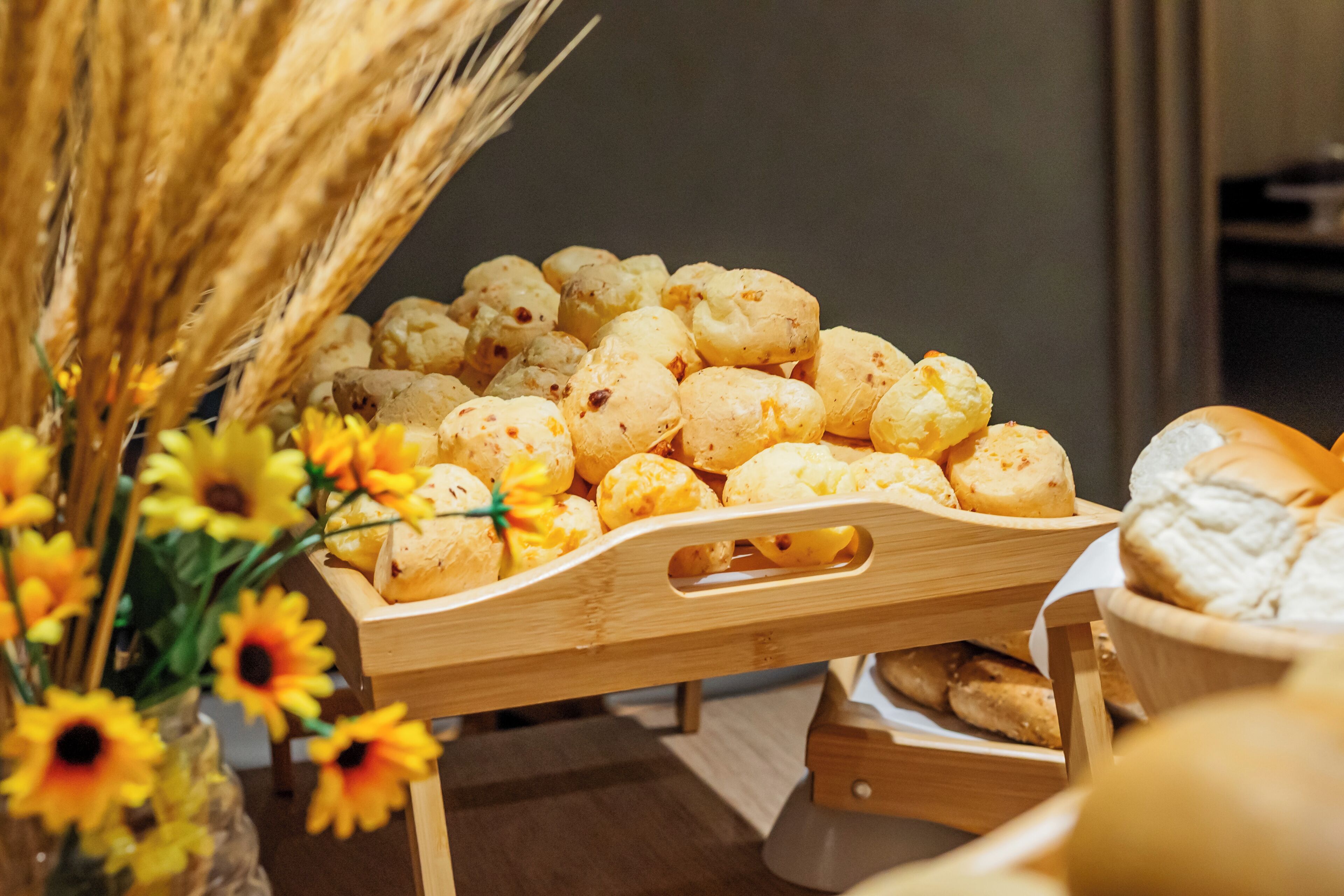 Una teca in legno esposta con diversi dolci e pane, insieme a un vaso di girasoli e spighe di grano.