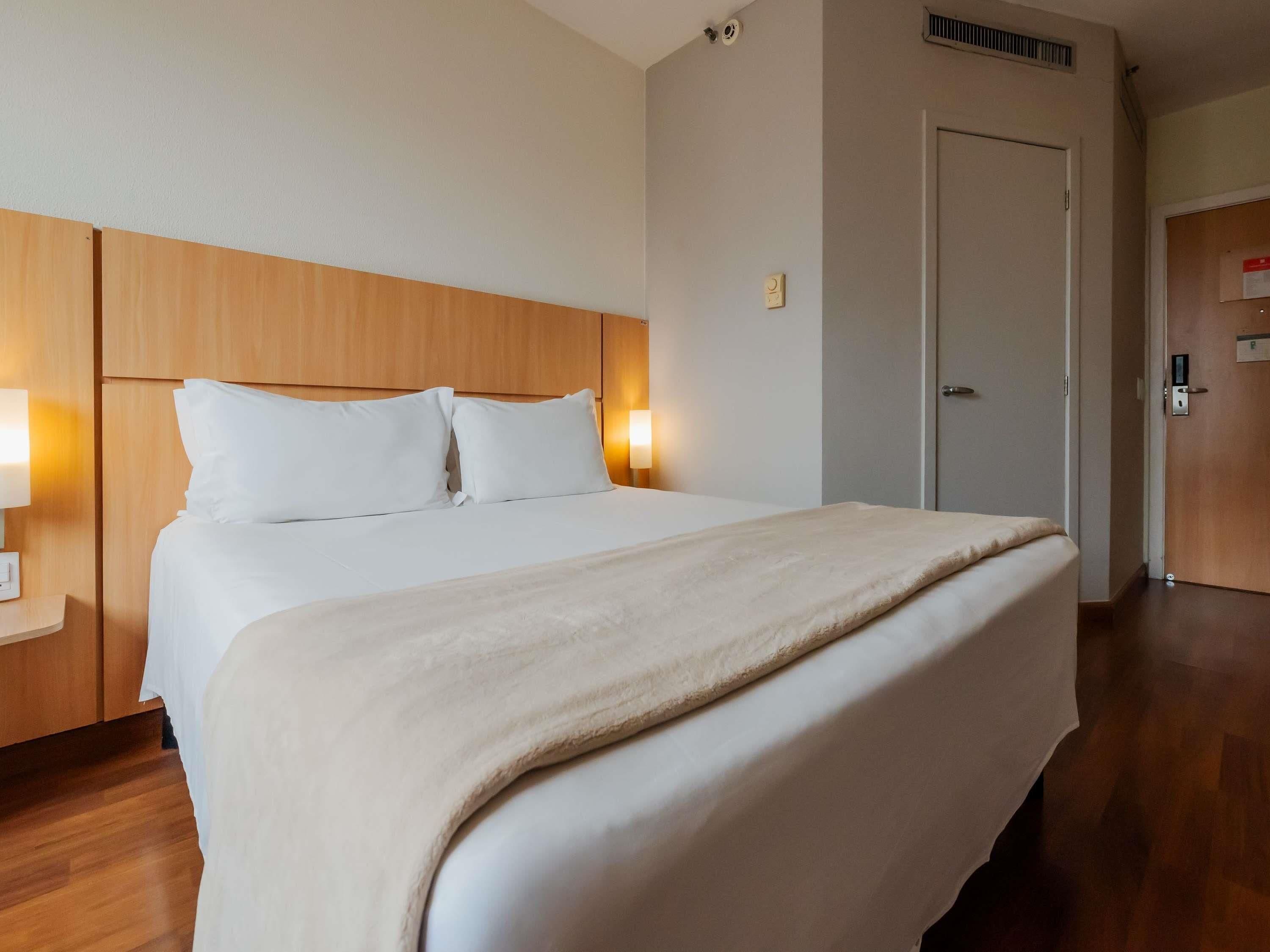 Una habitación de hotel con una cama grande, cabecera de madera, lámparas de noche y una puerta con cerradura.