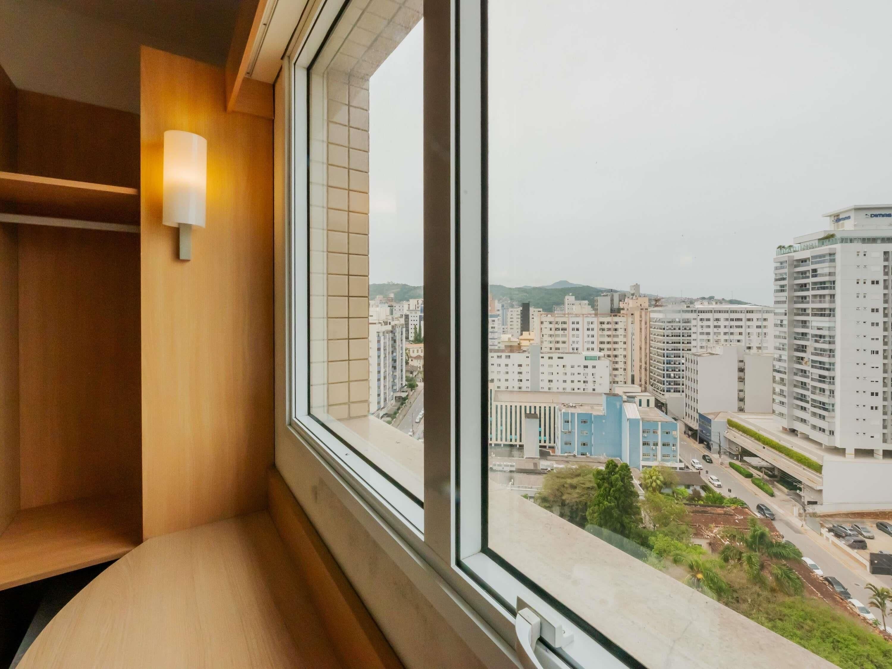 Una habitación con un ventanal grande, un banco de madera y una lámpara fijada a la pared.