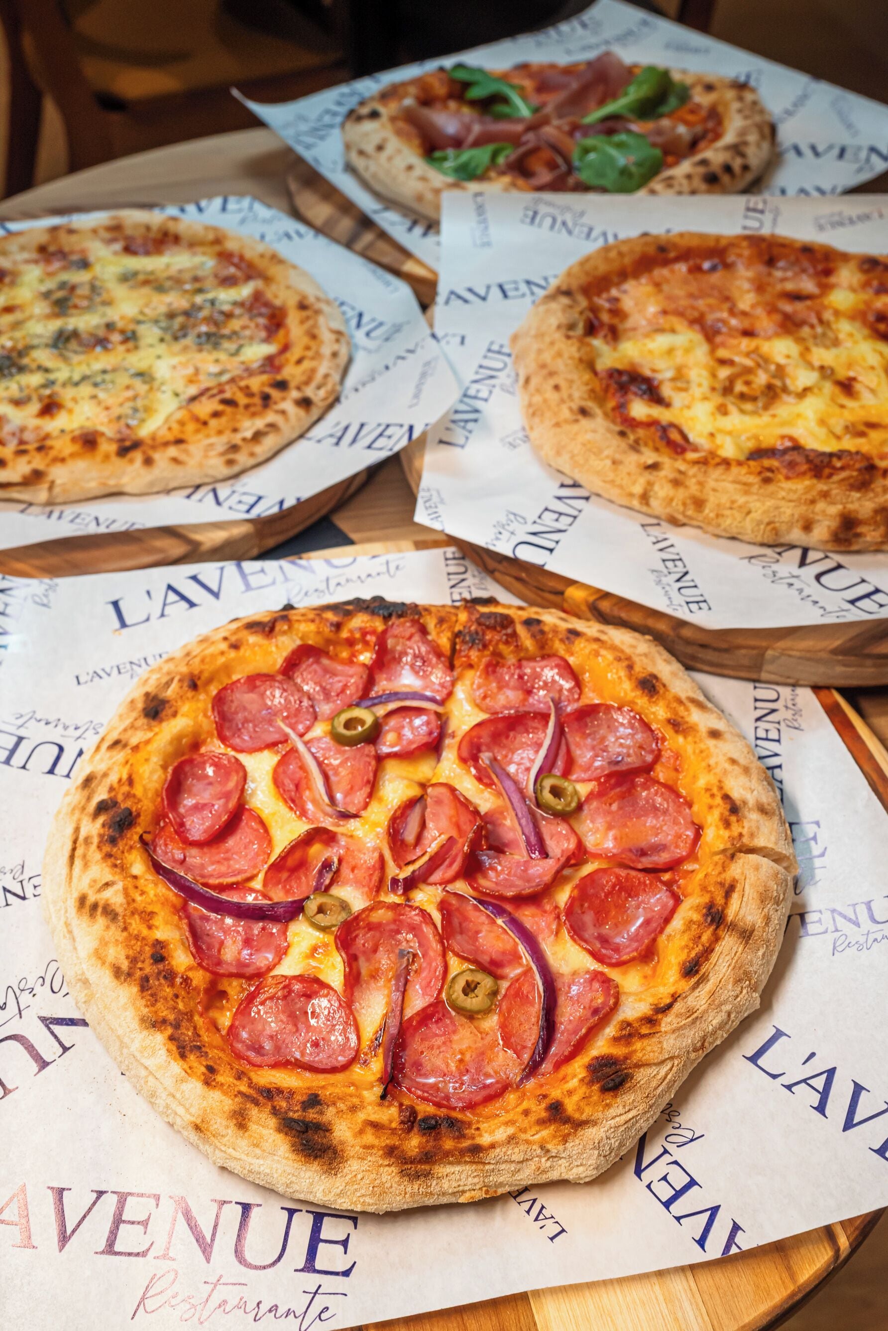 Three pizzas on a wooden table with menus underneath.