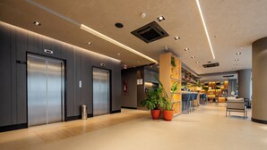 A modern hotel lobby with elevators, a reception desk, and a seating area.
