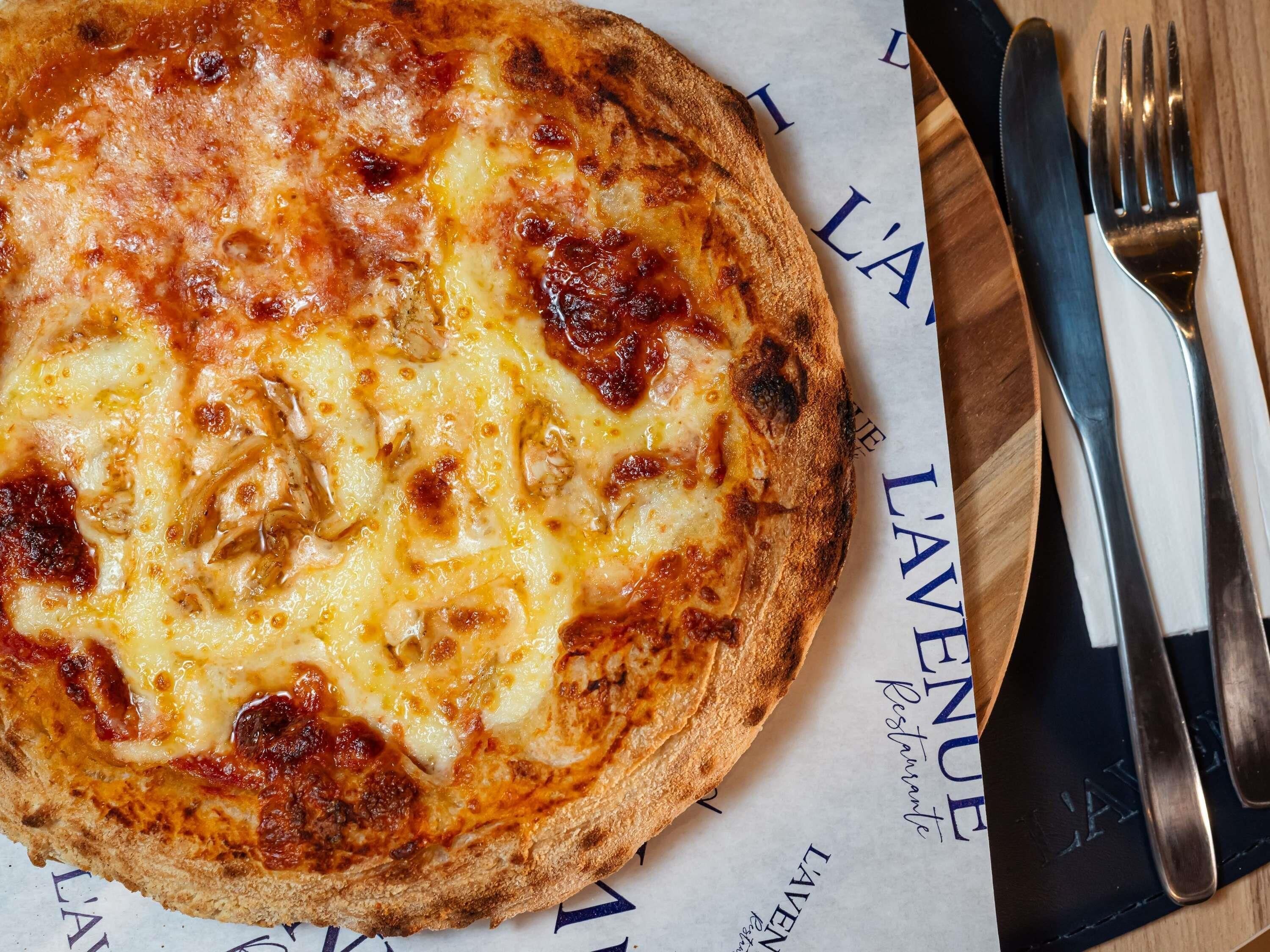 Una pizza su un tagliere di legno, con un tovagliolo e posate accanto.