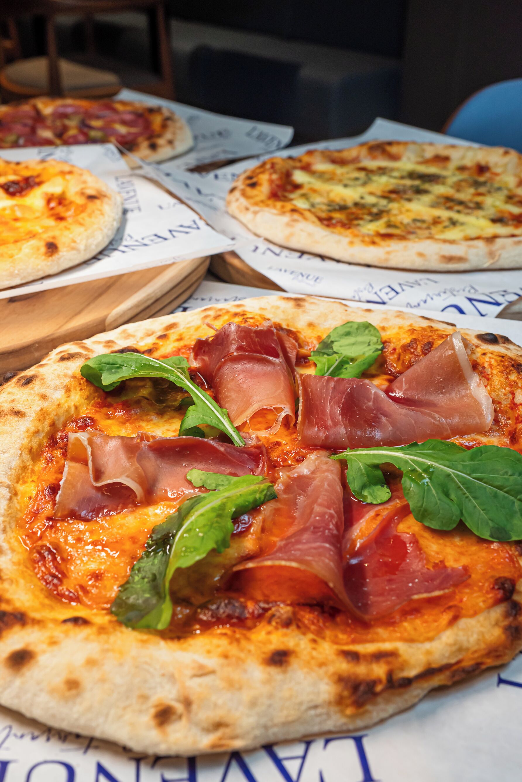 Una pizza con prosciutto e rucola su un tagliere di legno.