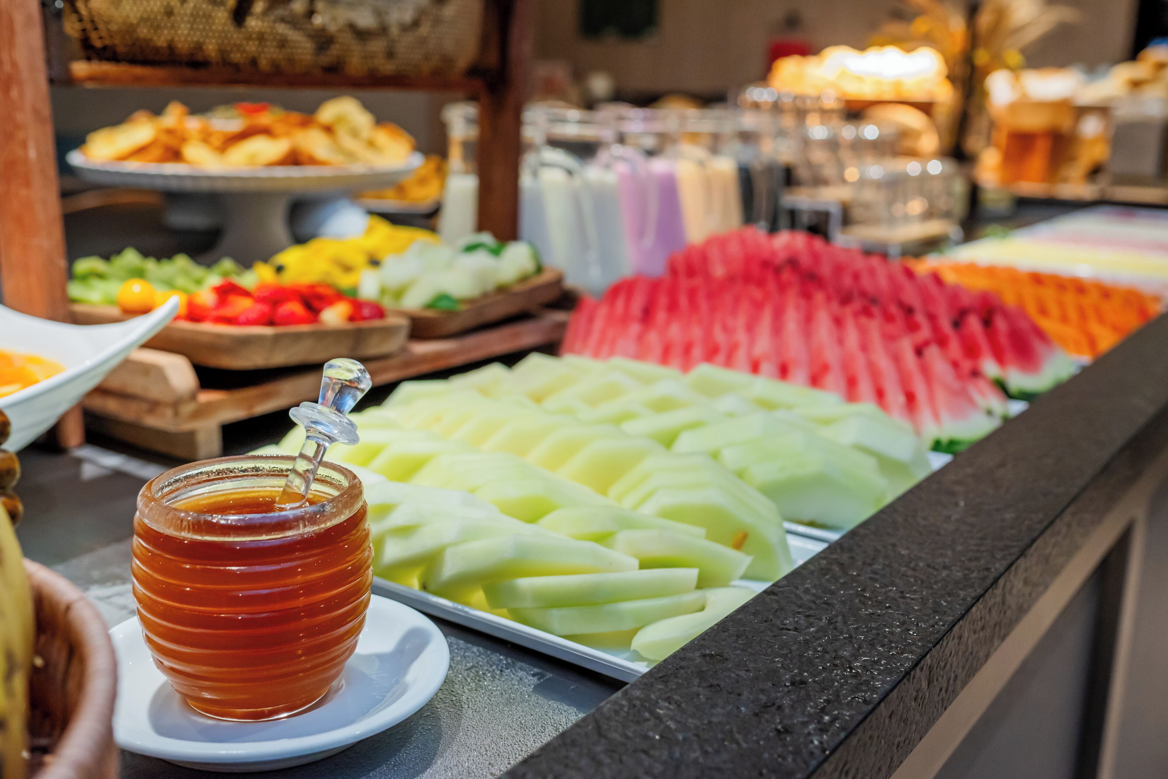 Buffet com diversos alimentos, incluindo frutas fatiadas e um pote de mel.