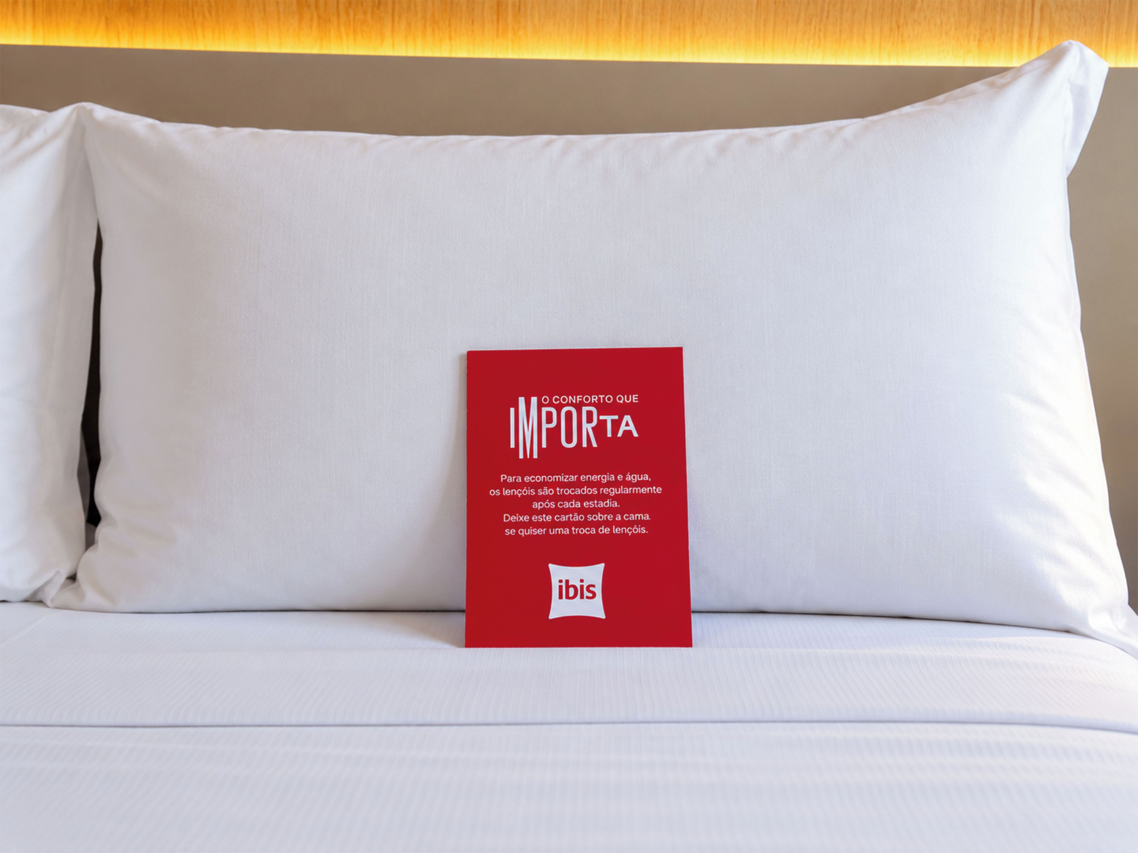 A bed with white bedding and a red informational card on it.