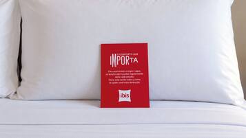 A bed with white bedding and a red informational card on it.